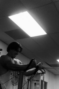 A muscular man working out in a gym using resistance bands. Black and white photography.