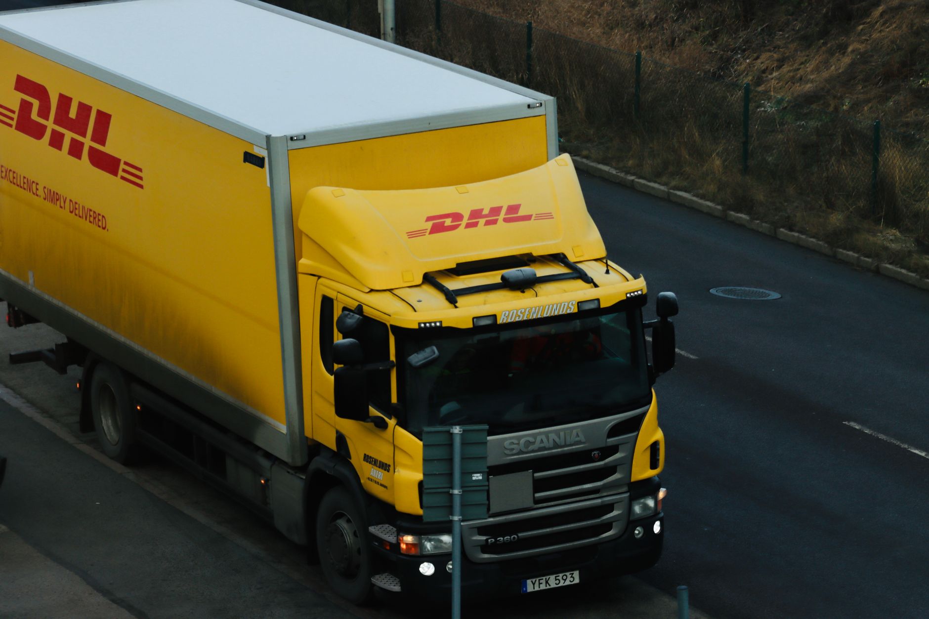 Yellow DHL delivery truck driving along a city road showcasing logistics in action.
