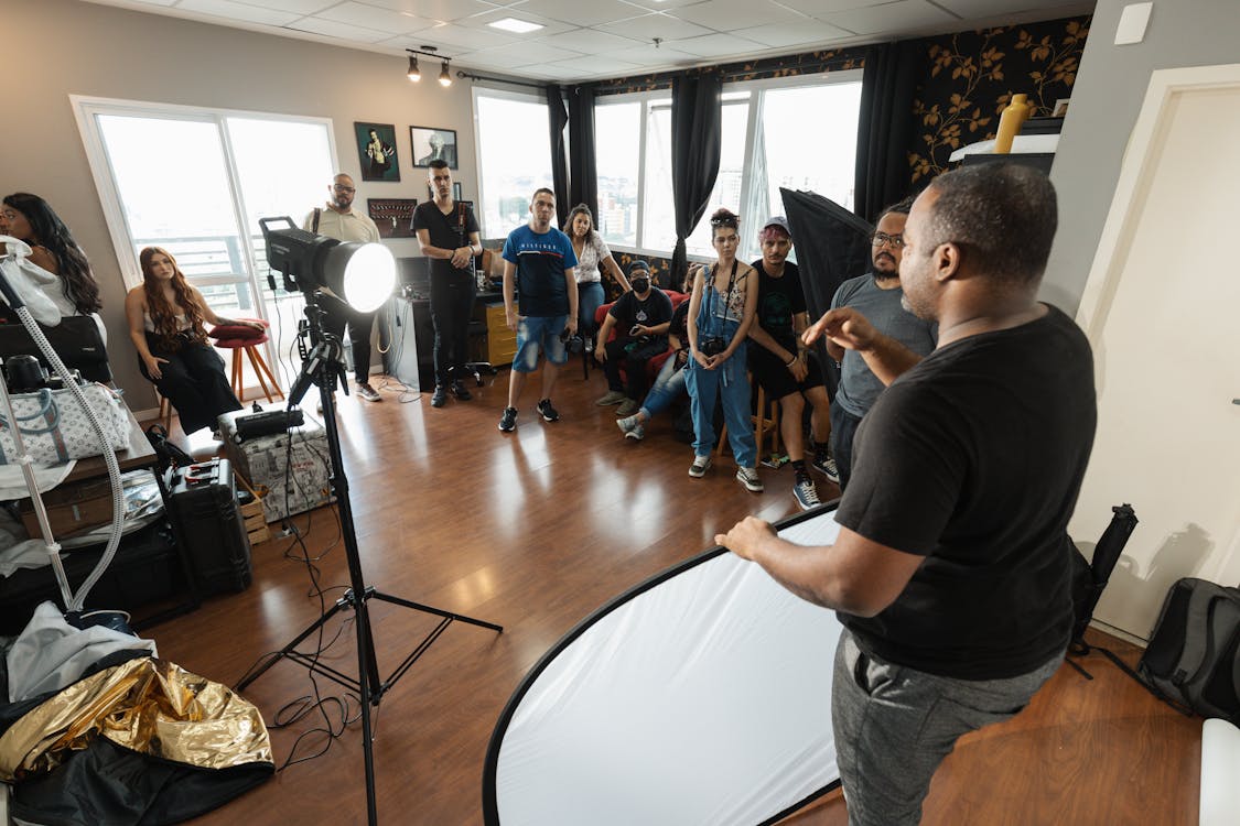 A man addresses a gathering, standing prominently in front of a diverse group of people who are focused on him.