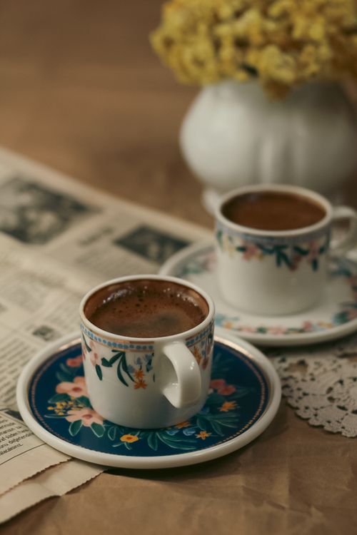 Free Two floral coffee cups on a table with a newspaper, evoking a retro vibe. Stock Photo