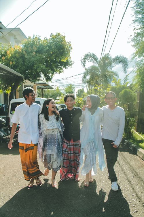 Free Group of friends joyfully walking on a sunlit city street, wearing traditional attire. Stock Photo