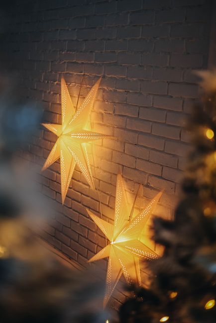 Fotomural Estrellas de papel iluminadas adornan una pared de ladrillos blancos, creando un ambiente festivo y acogedor en el interior.