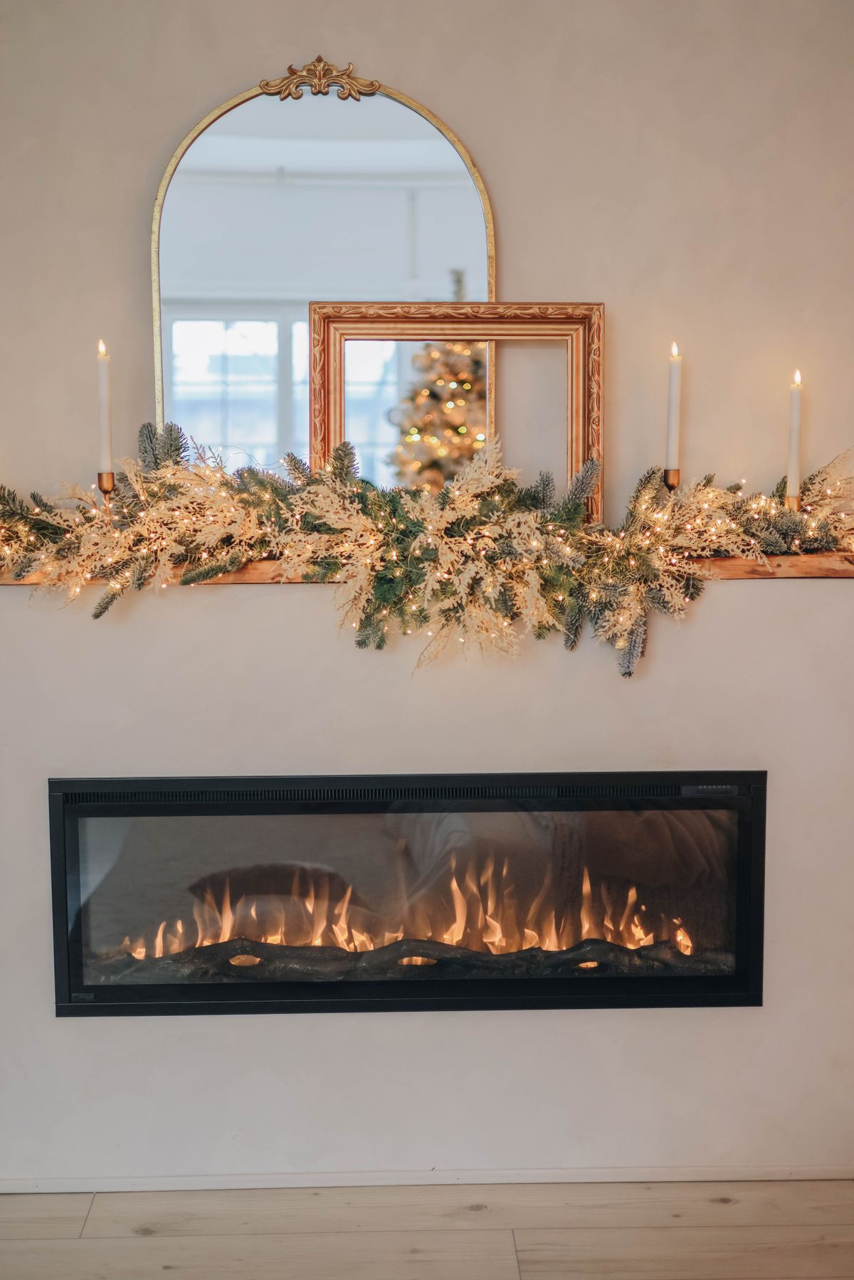 Fireplace mantel with framed mirrors reflecting Christmas candles and greenery