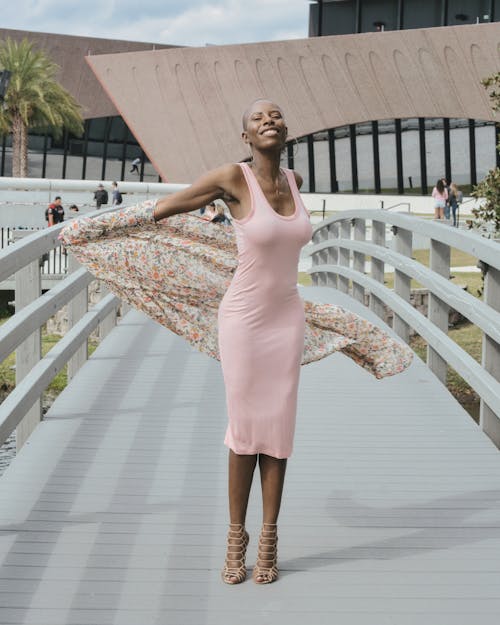 Woman in a Pink Dress and Floral Gown Standing on a Footbridge 