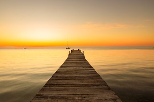 Free Wooden pier extends into tranquil sea at sunset in Belize, creating a warm, peaceful scene. Stock Photo