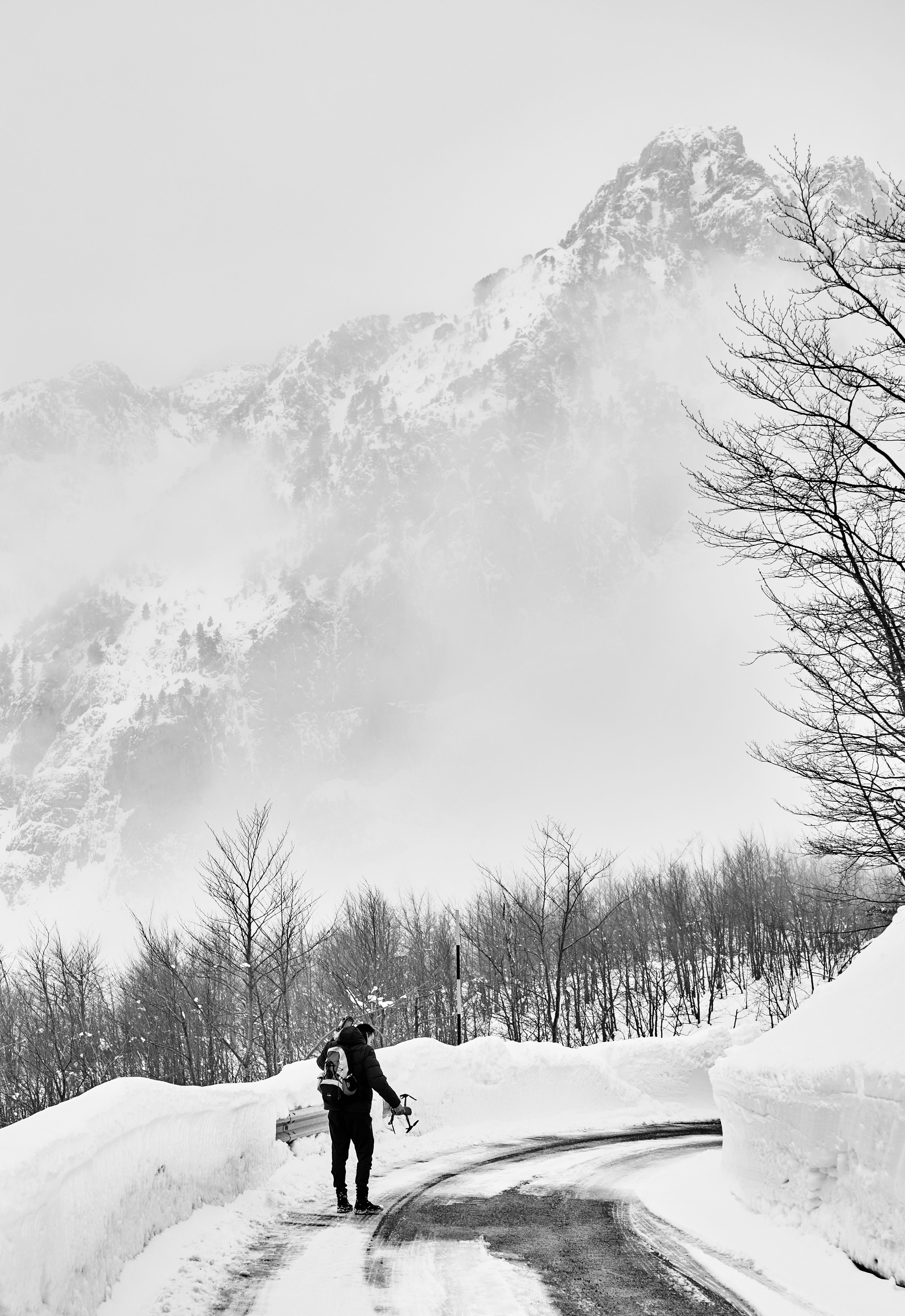 A lone hiker traverses a snowy road in the foggy mountains of Bogë, Albania.