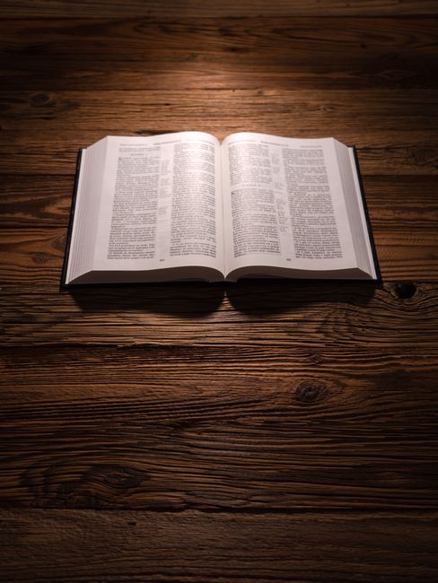 An open Bible resting on a wooden table, illuminated by soft lighting, creating a serene ambience.
