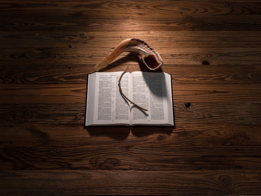 An open Bible on a wooden table with a shofar and twig, captured in a warm, dramatic lighting.