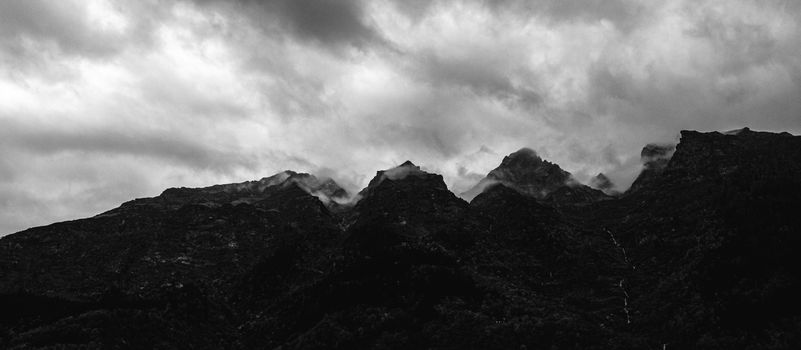 Black and white photo of a rocky mountain range under dramatic cloudy skies.
