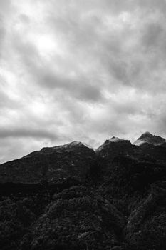 Moody black and white photograph of cloud-covered mountain peaks.