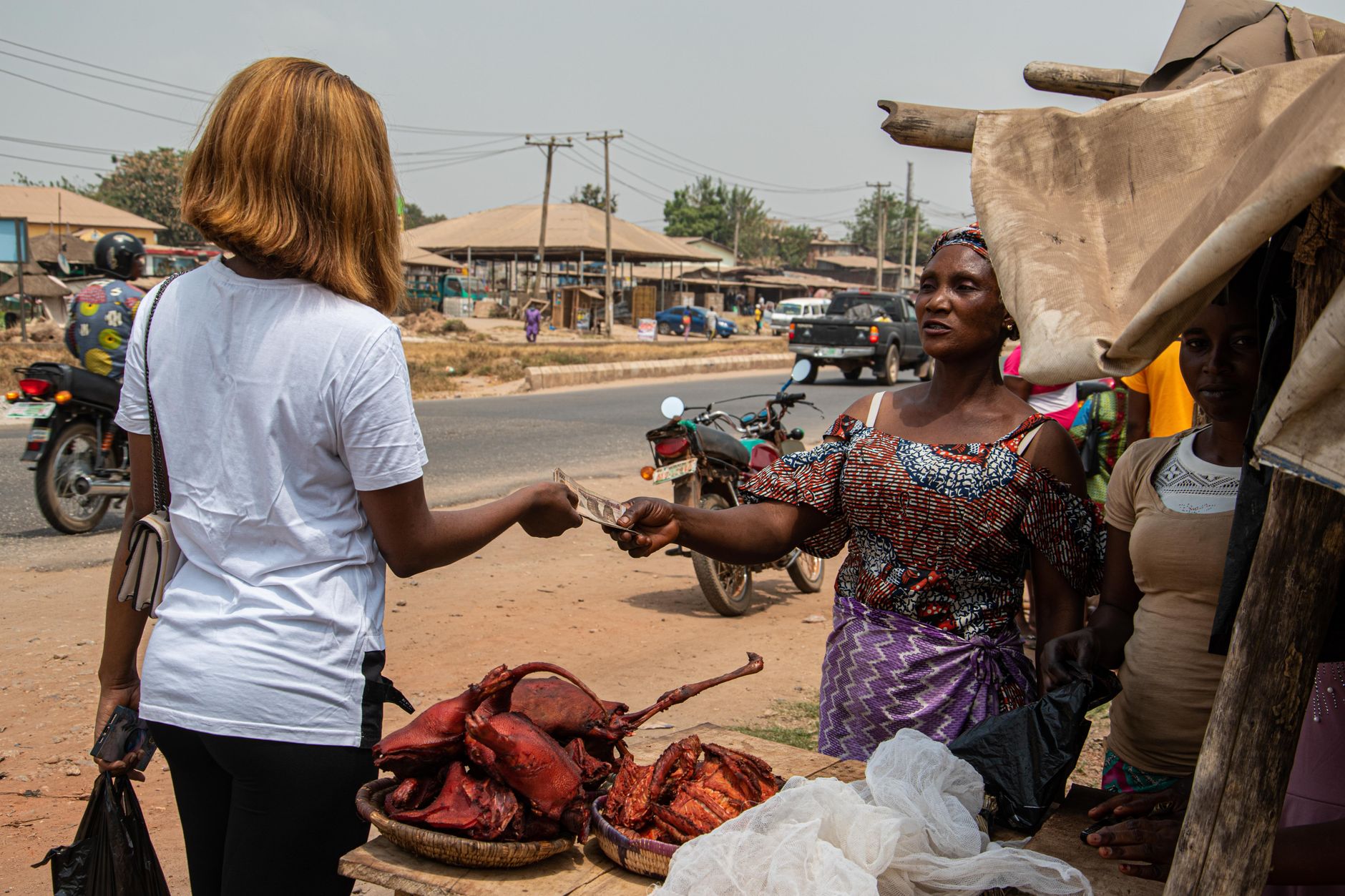 A woman purchasing meat from a vendor at an outdoor market in a small African town.
