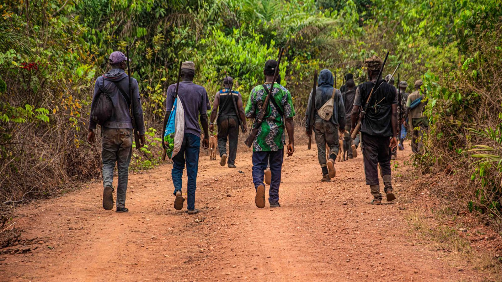 People carrying rifle while walking on the dirt road, Ghana