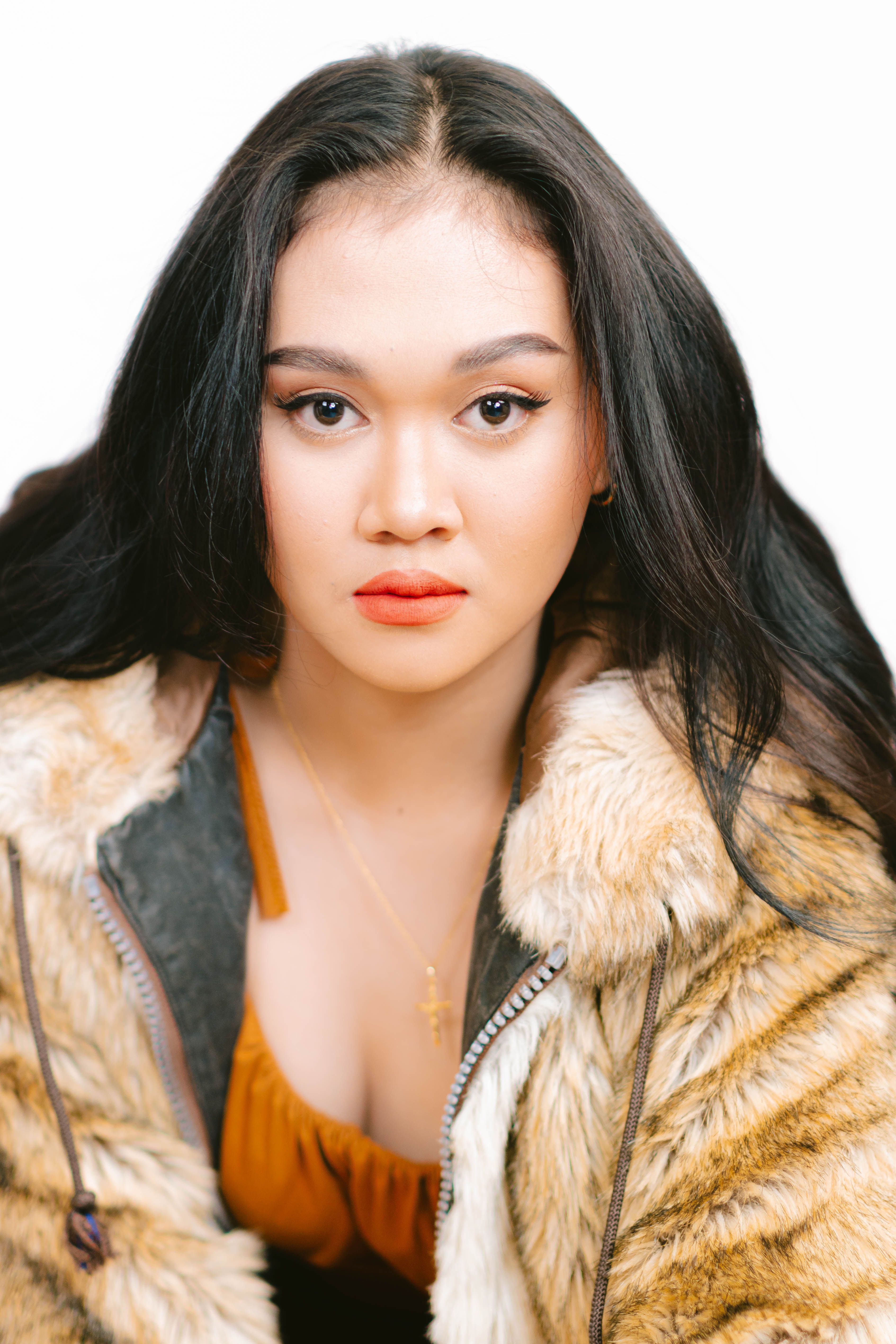Fashion portrait of a woman wearing a fur jacket, showcasing bold makeup with a white background.