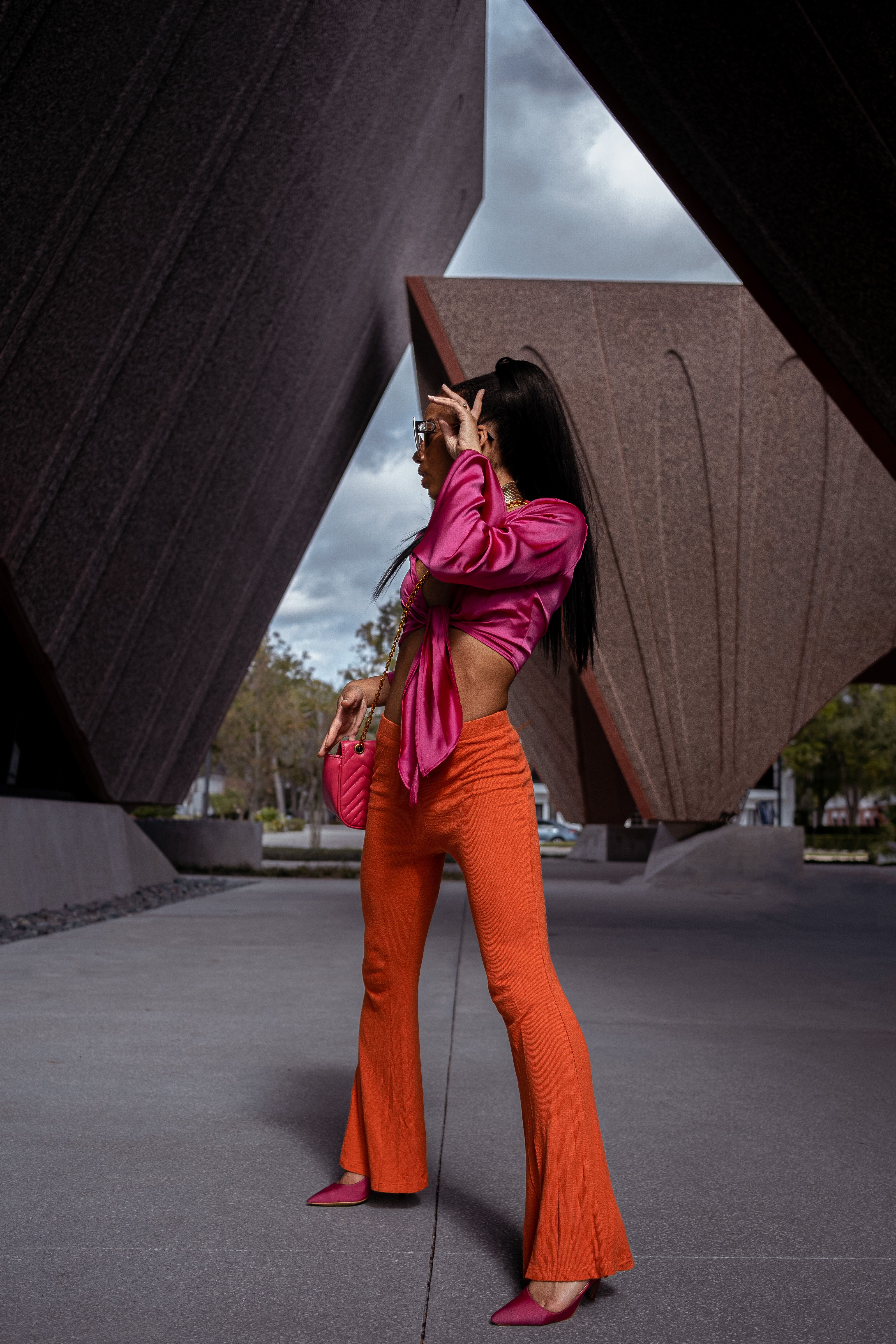 Stylish woman in vivid pink blouse and orange pants posing elegantly outdoors.