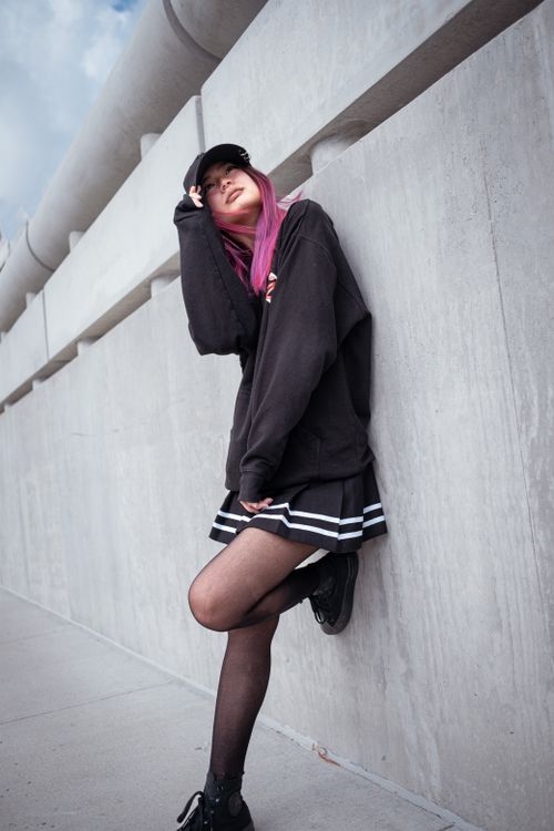 Free A stylish woman with pink hair leans against a concrete wall, wearing a black jacket and mini skirt. Stock Photo