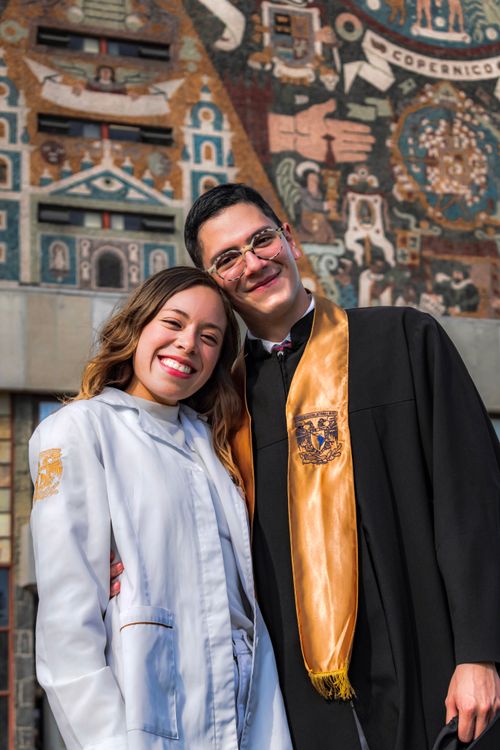 Free Young graduates in cap and gown smiling in front of a mural. Stock Photo