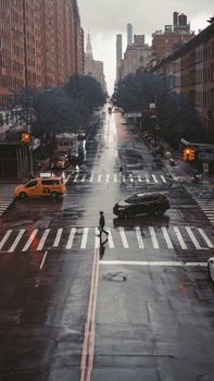 A rainy street view of New York City with pedestrians and cars at a crosswalk.