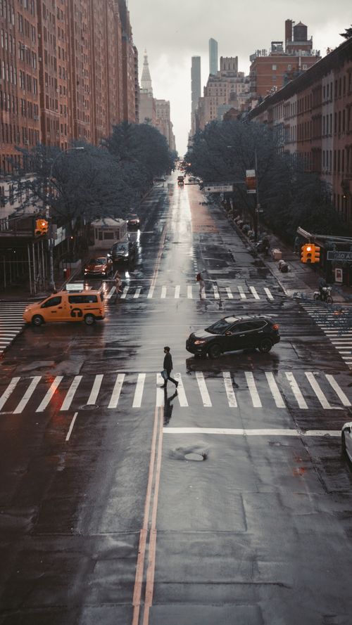 Free A rainy street view of New York City with pedestrians and cars at a crosswalk. Stock Photo