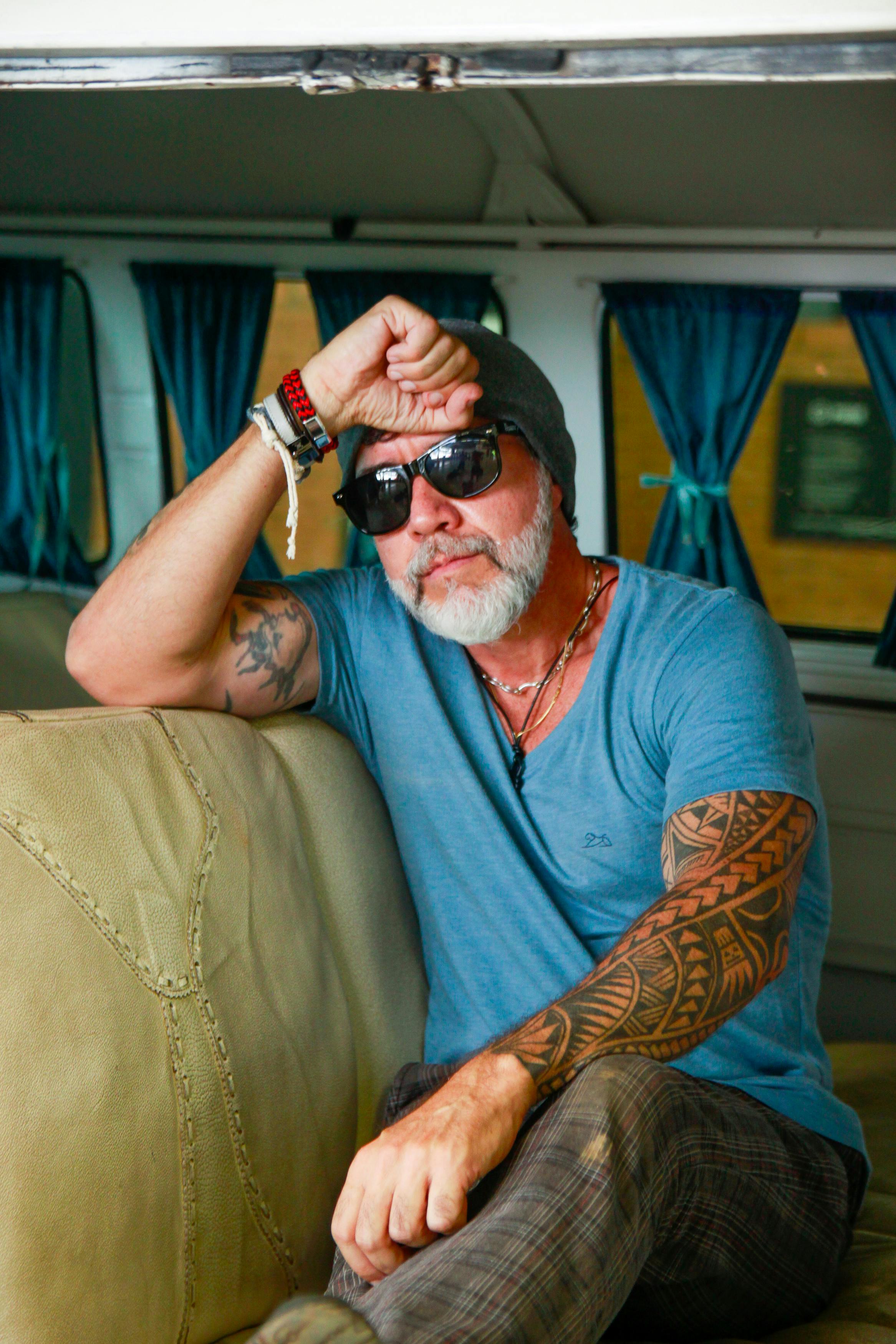 Bearded tattooed man in sunglasses and hat inside a vintage camper van. Cool and casual style.
