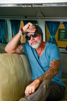 Bearded tattooed man in sunglasses and hat inside a vintage camper van. Cool and casual style.
