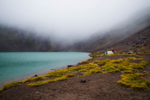 山间湖泊雾气宁静，岸边有露营者，展现了大自然的宁静