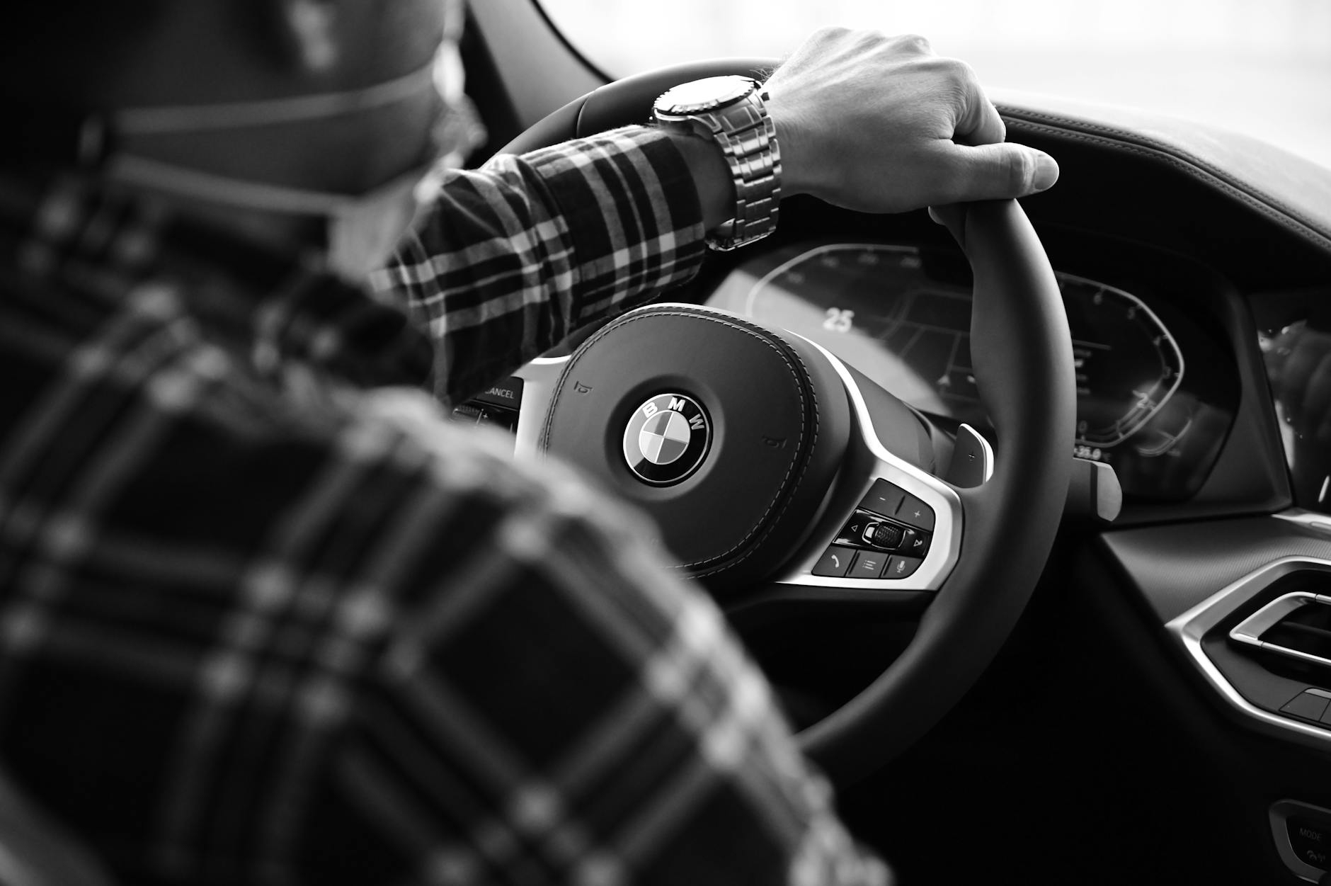 Close-up of a driver's hand on a steering wheel in black and white.