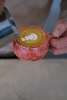 Close-up of a barista pouring frothy milk to create latte art in a cafe.