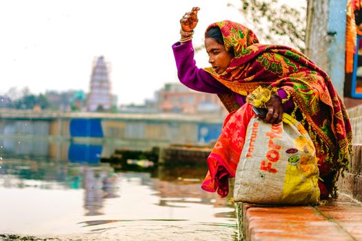 A woman performs a traditional ritual by a river in India, displaying cultural and religious practices.