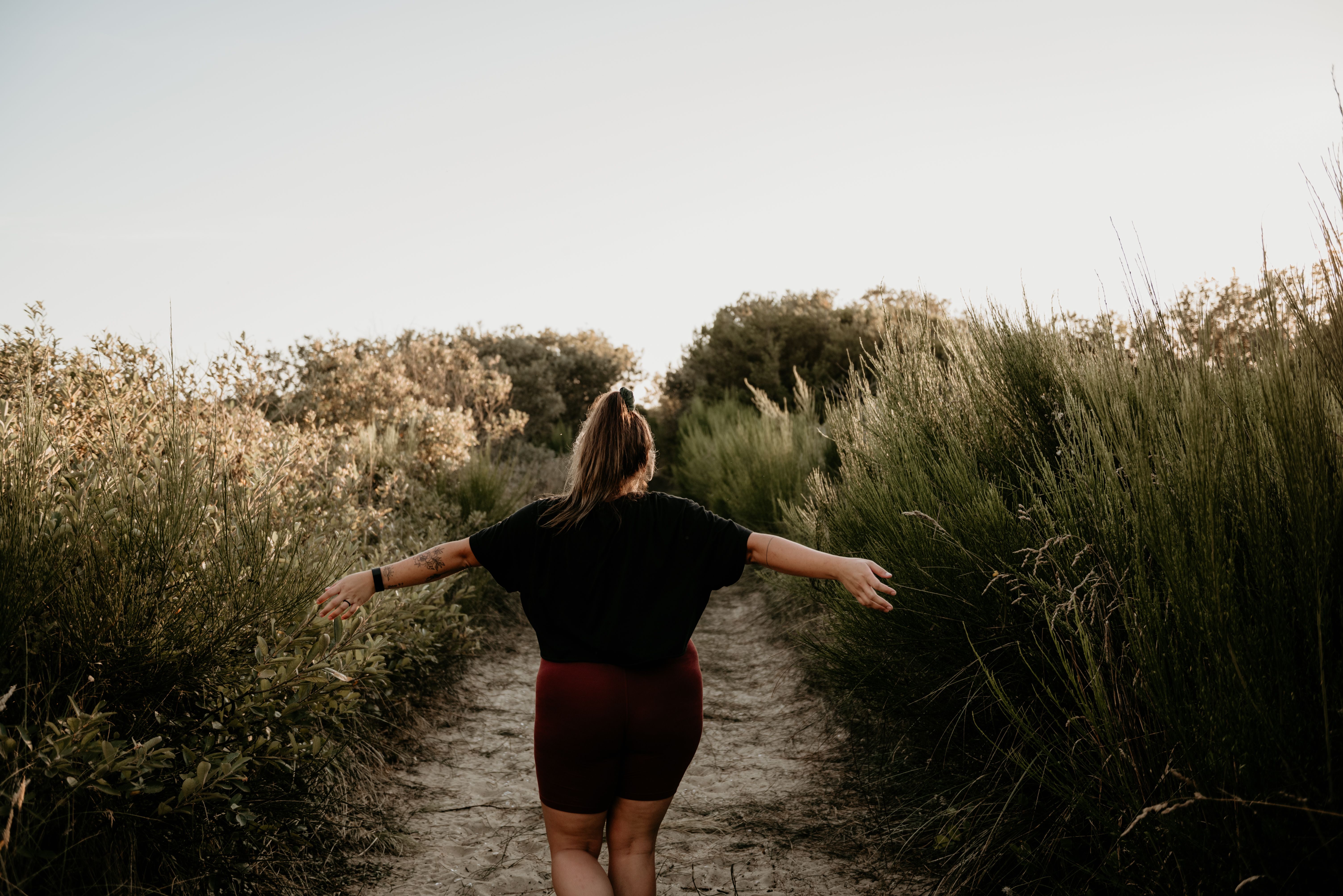 Back view of a woman walking on a rural path in summer with tall grass around.