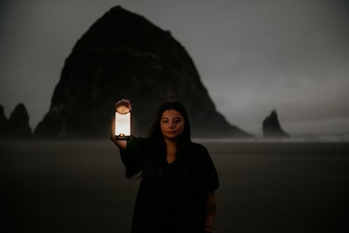 Woman Standing with a Lantern in her Hand on a Beach at Night 