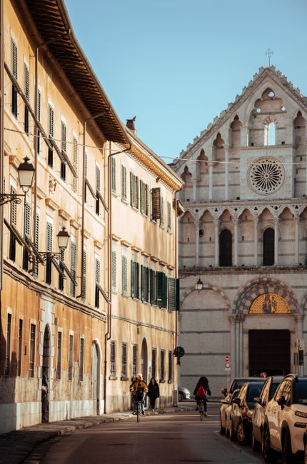 Street view of a gothic church facade in Pisa, Italy with surrounding buildings.