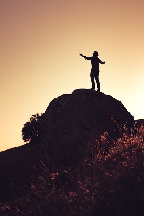 Silhouette of Person with Arms Stretched on Rock