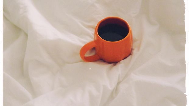 Cozy orange coffee mug resting in soft white bedding for a warm, inviting morning vibe.