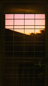 A grated window captures a stunning sunset in Yangon, Myanmar, with warm colors.