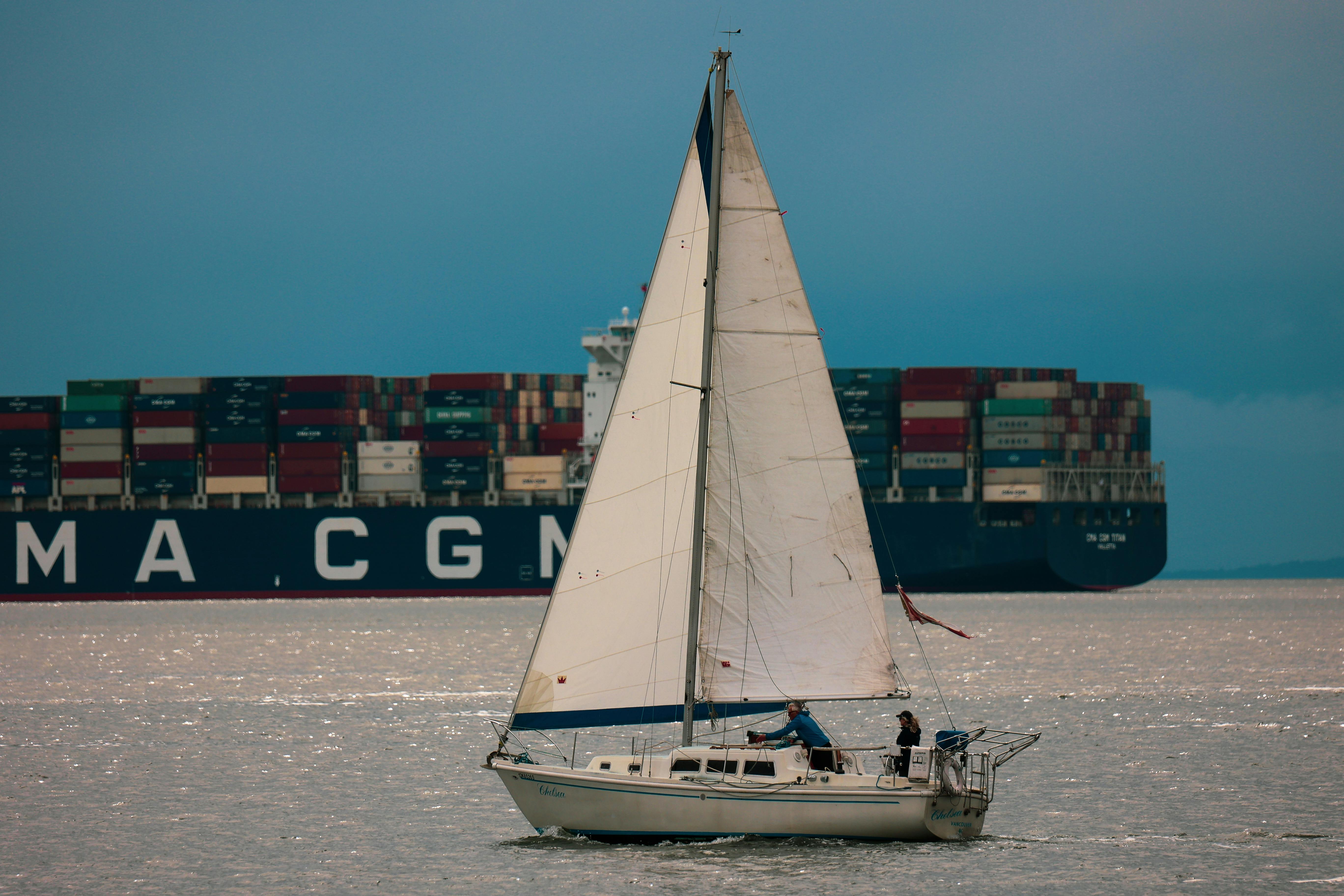Sailboat cruising in front of a cargo ship in Vancouver, Canada.