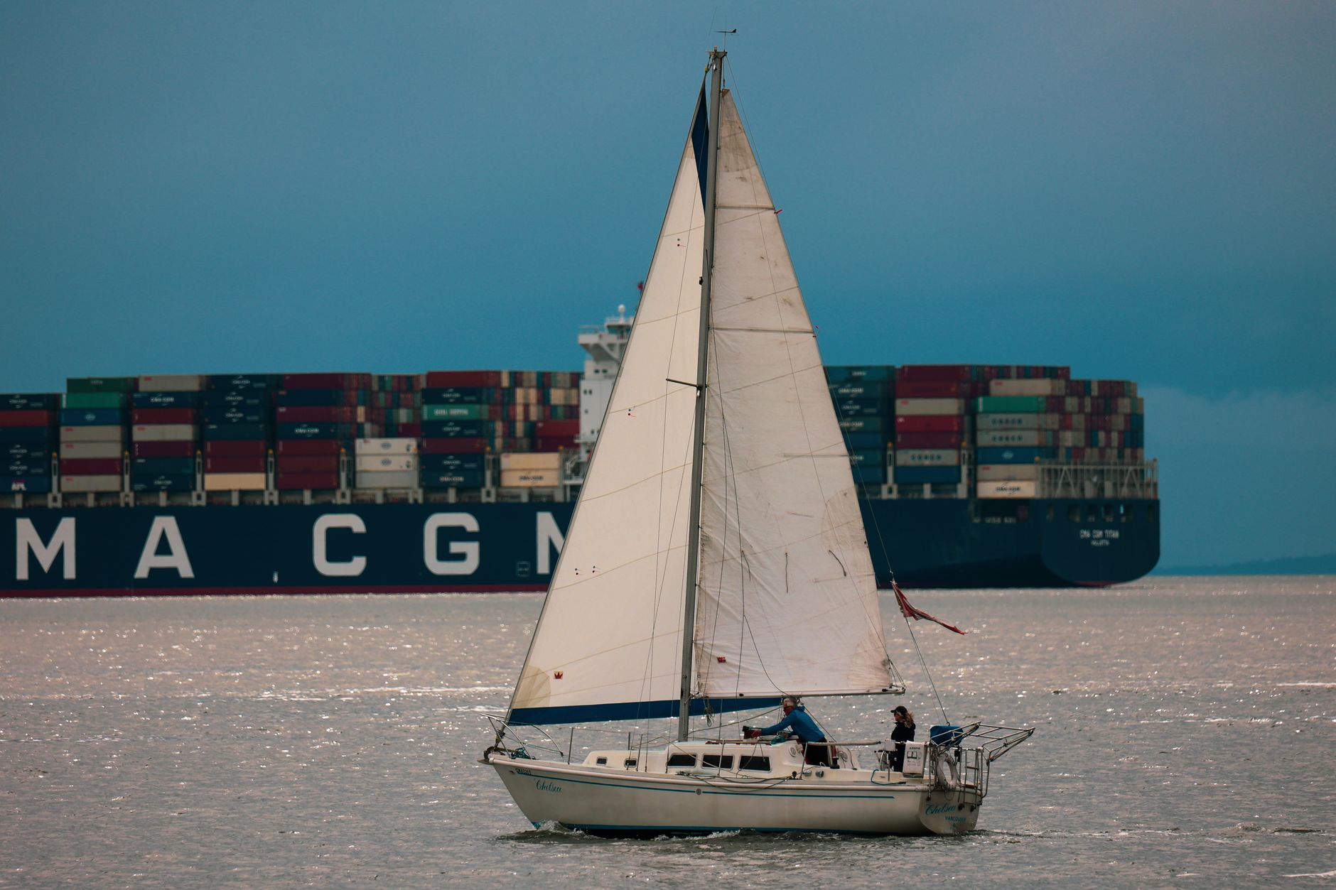 Sailboat cruising in front of a cargo ship in Vancouver, Canada.