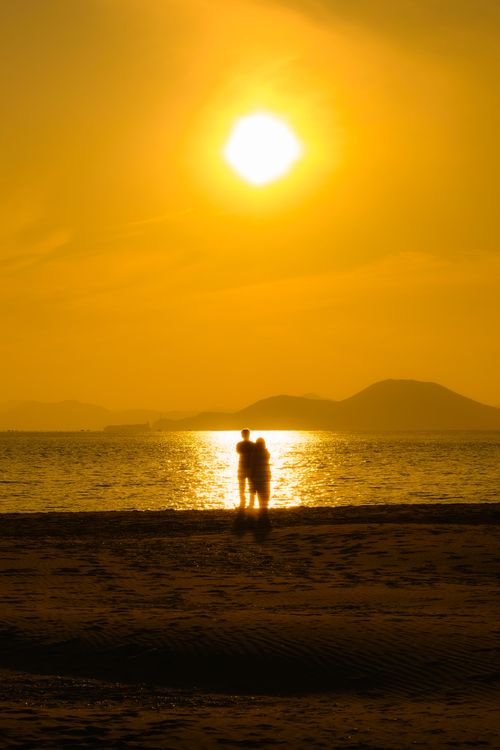 Free Silhouetted couple embracing at the beach during a stunning golden sunset. Stock Photo
