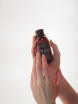 Stylish close-up of hands holding a cosmetic bottle against a white background, perfect for beauty and skincare themes.