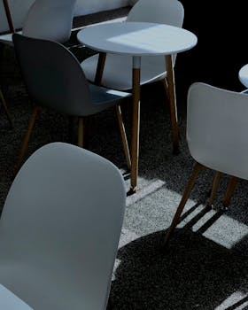 Empty modern cafe chairs and tables under sunlit indoors, creating dramatic shadows.