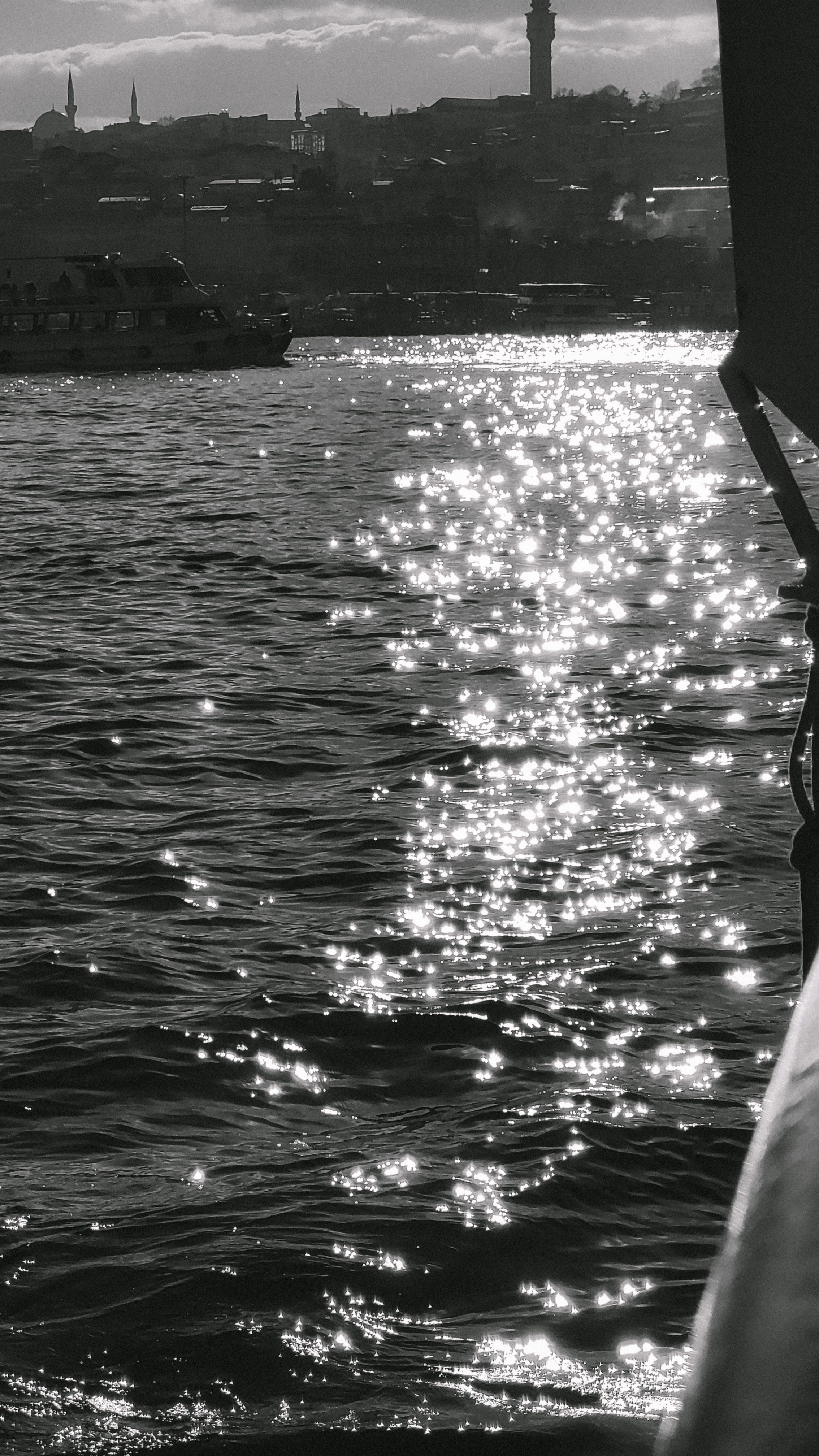 A black and white image of a shimmering harbor under sunlight, capturing serene water views.