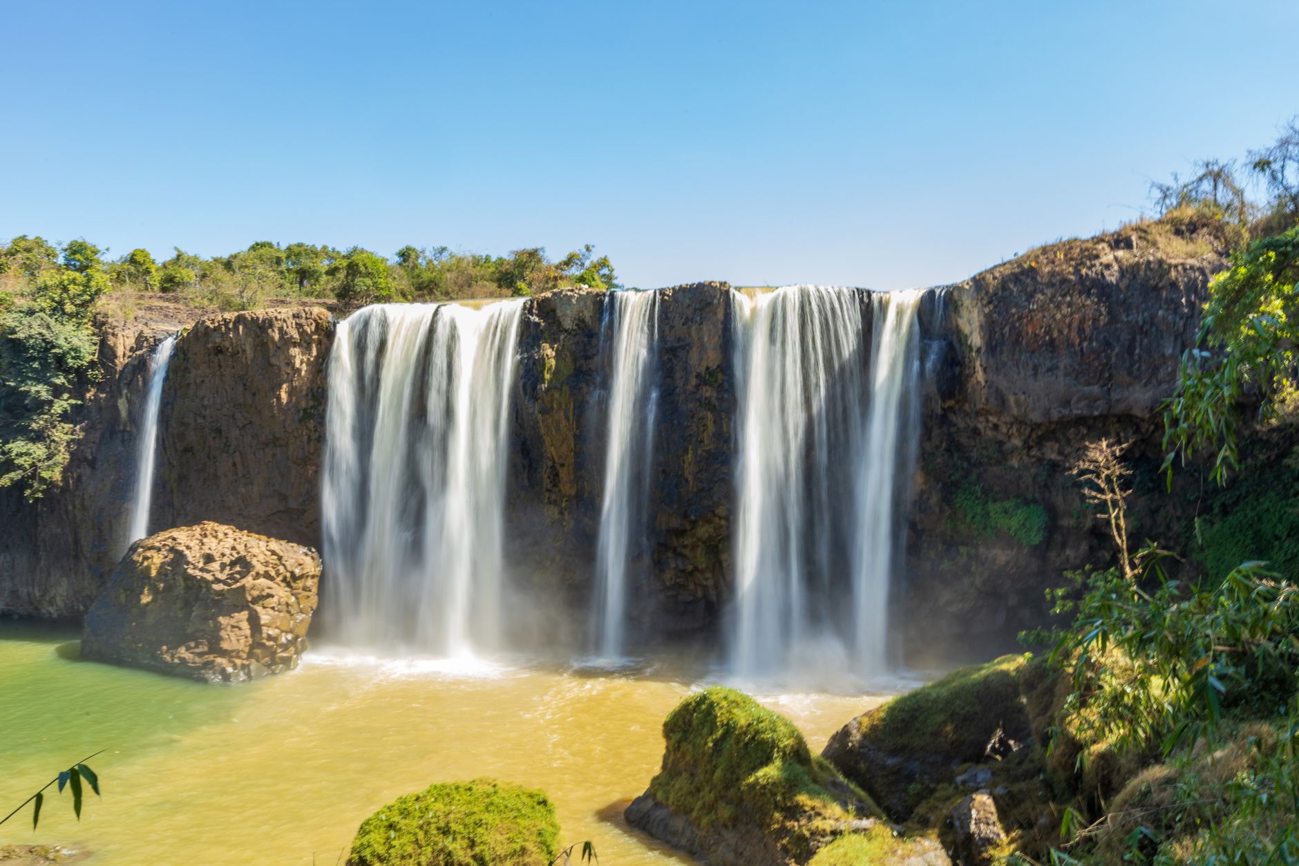 Stunning waterfall amidst lush greenery and rocky cliffs under a clear blue sky.