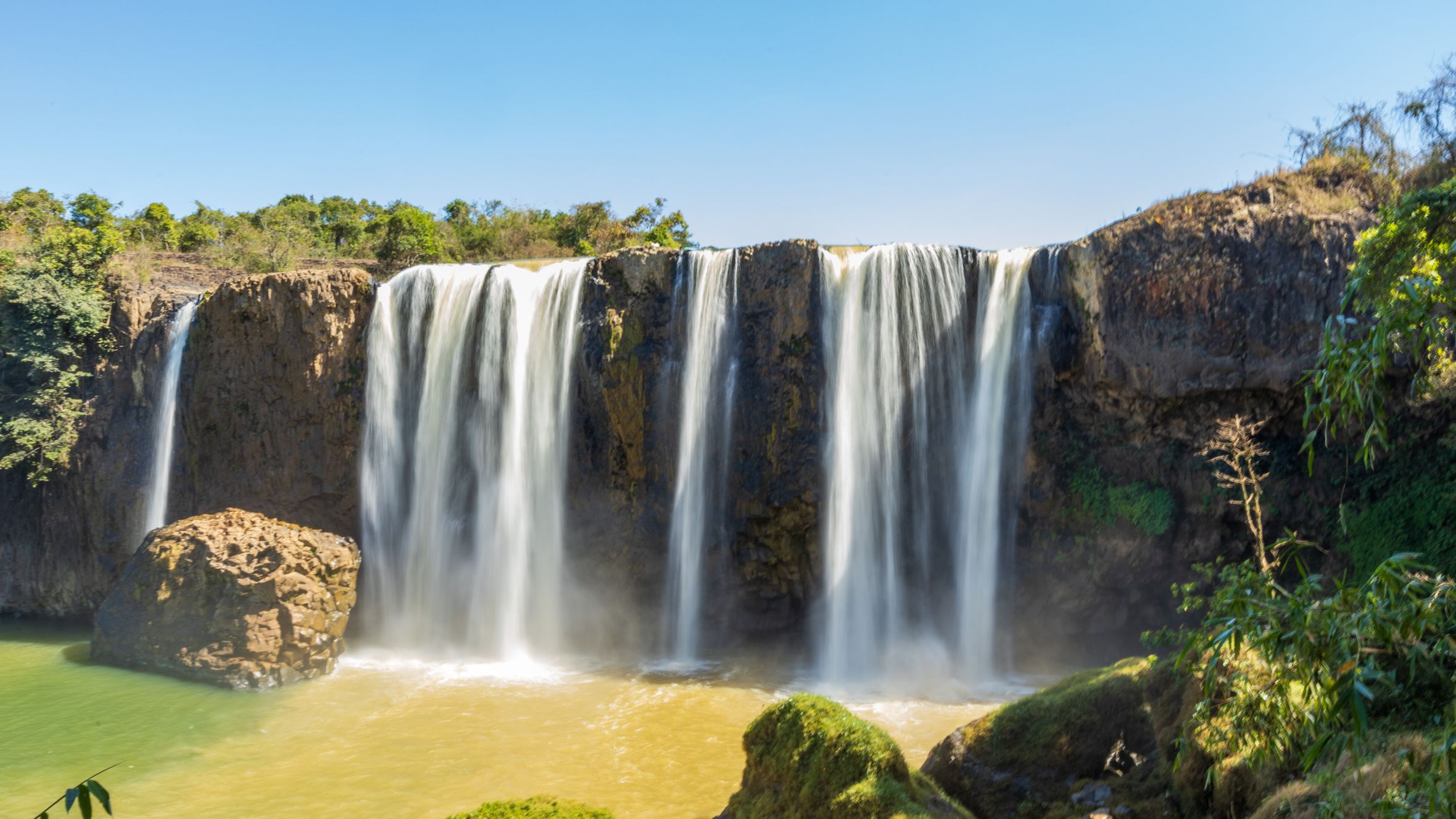 Stunning waterfall amidst lush greenery and rocky cliffs under a clear blue sky.