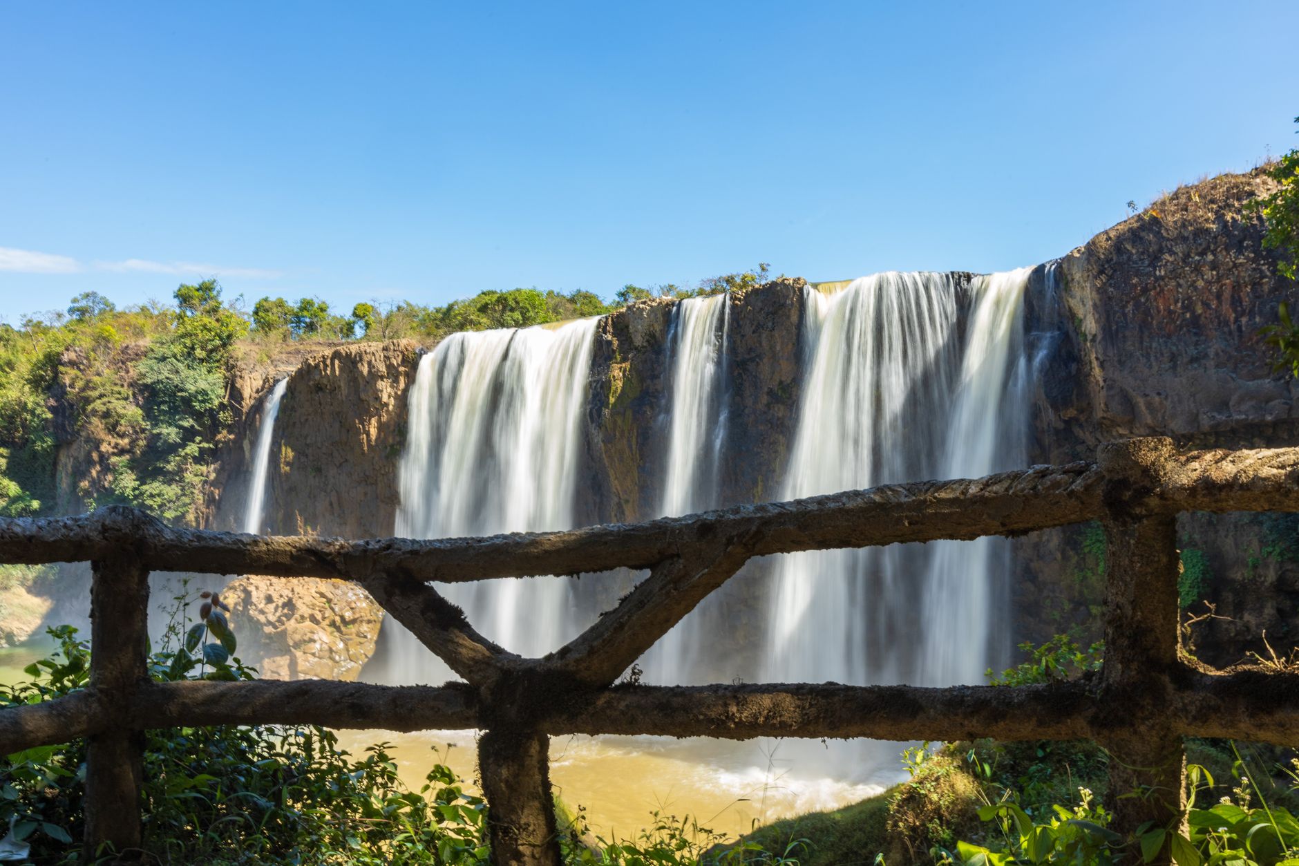 Stunning waterfall cascading over cliffs, viewed through rustic railings on a clear day.