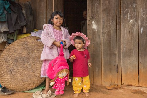 Free Two children standing indoors with a doll, depicting a rustic lifestyle. Stock Photo