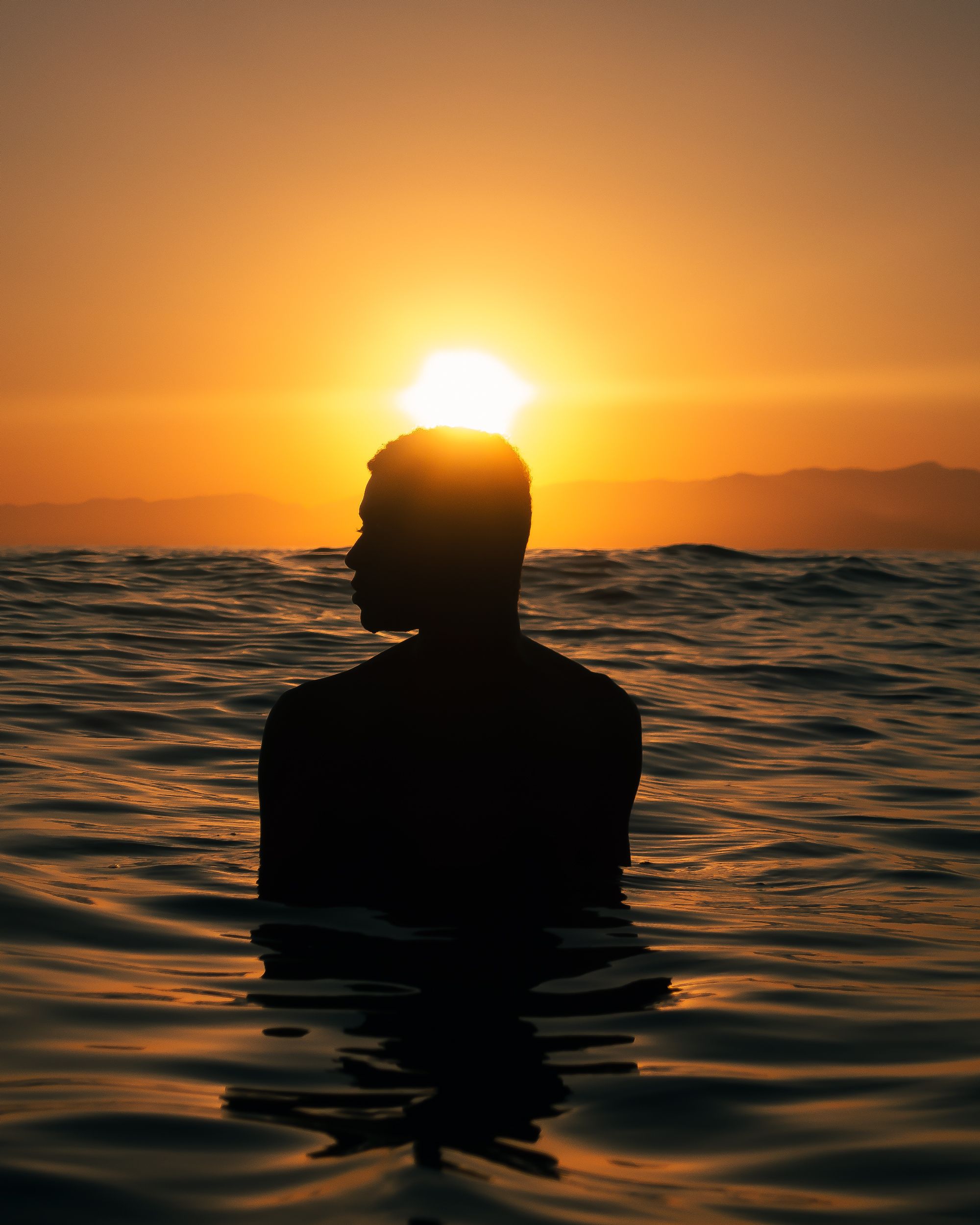 Silhouette of a Person Standing in the Sea with the Setting Sun Above ...