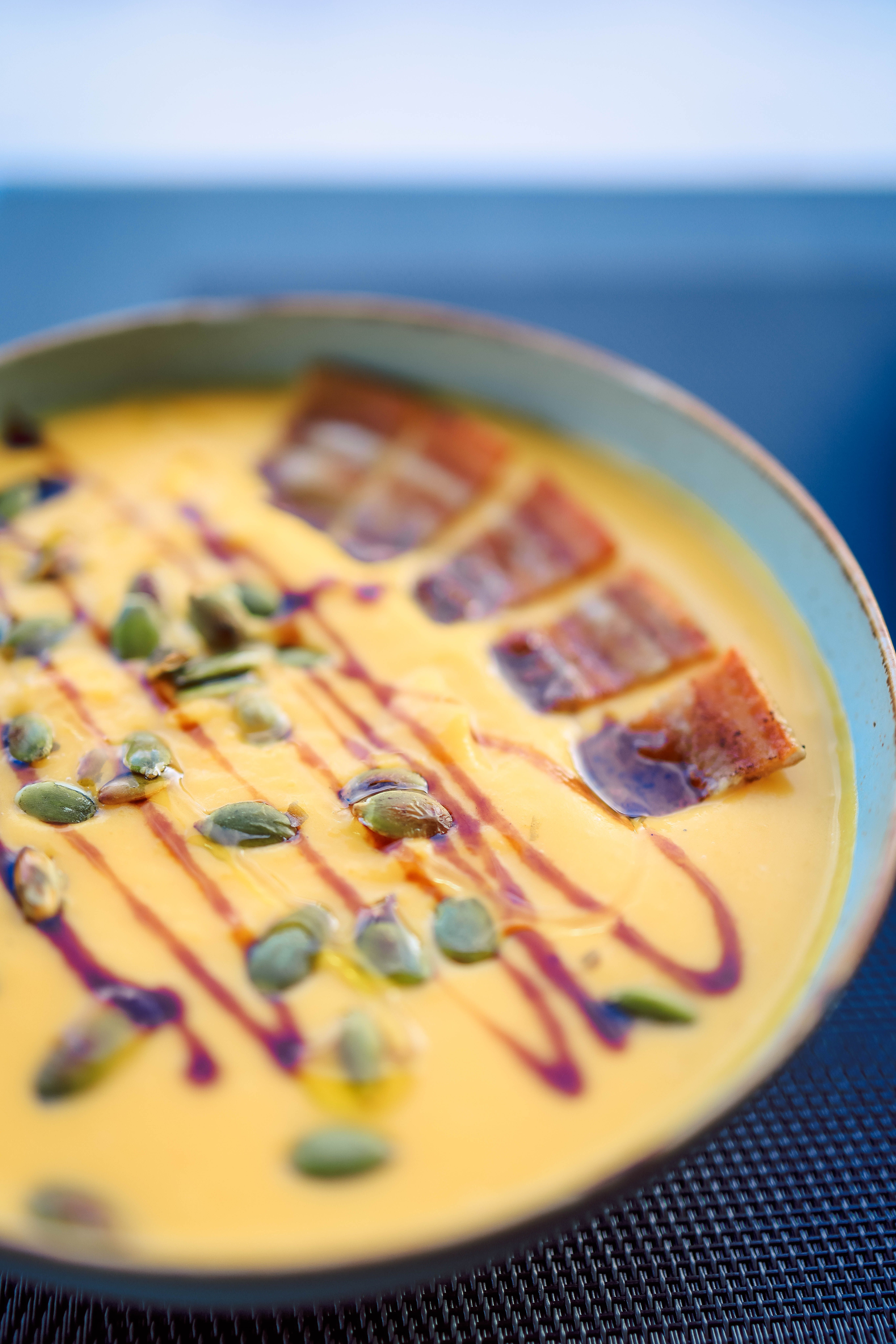 Close-up of creamy pumpkin soup topped with bacon strips and seeds, elegantly presented in a bowl.