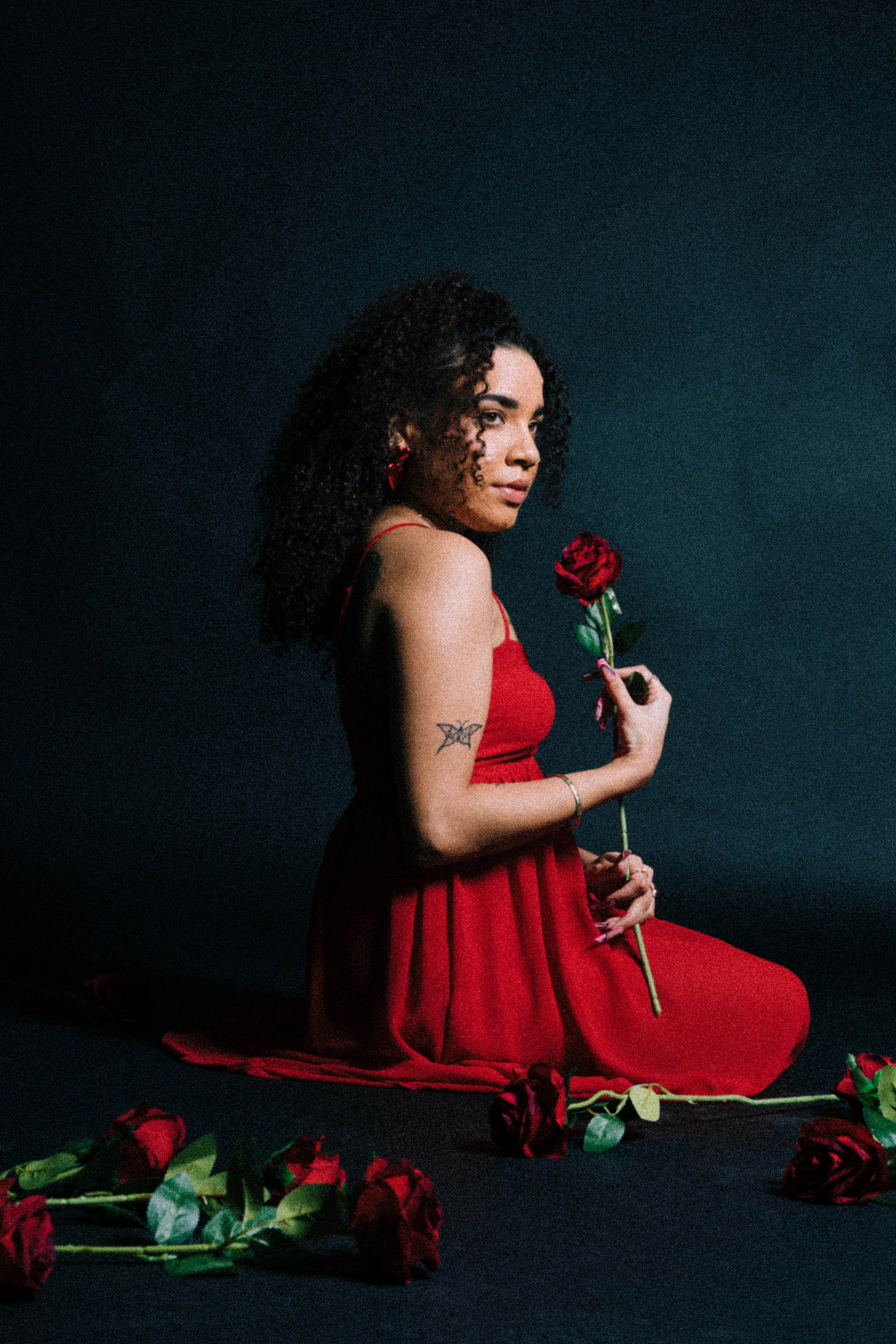 Portrait of a woman in a red dress holding roses, studio setting.