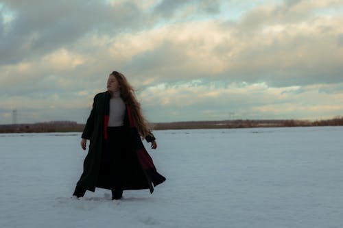 Woman in a Dark Green Coat and a Long Red and Black Scarf on a Frozen Lake