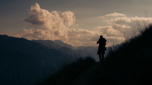 Free A lone hiker silhouetted against dramatic clouds and mountain scenery at twilight. Stock Photo
