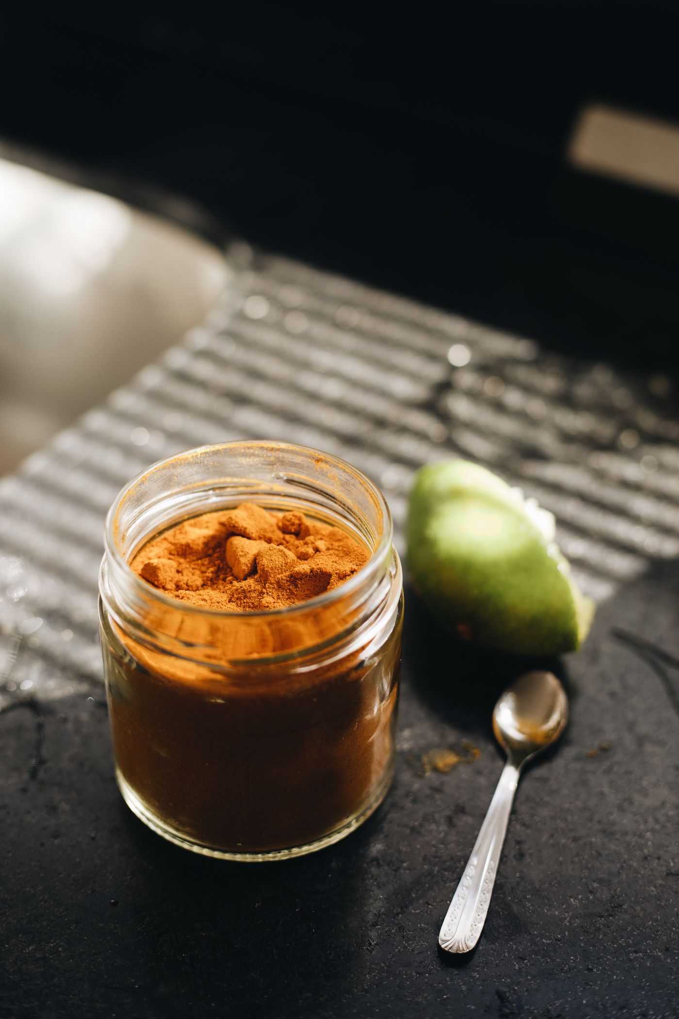 A glass jar of turmeric powder beside a spoon on a dark kitchen surface